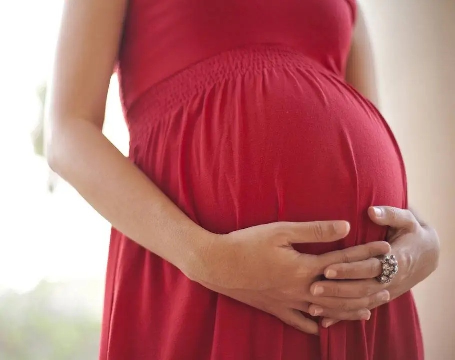 Symbolbild einer schwangeren Frau im roten Kleid, die sich den Bauch hält